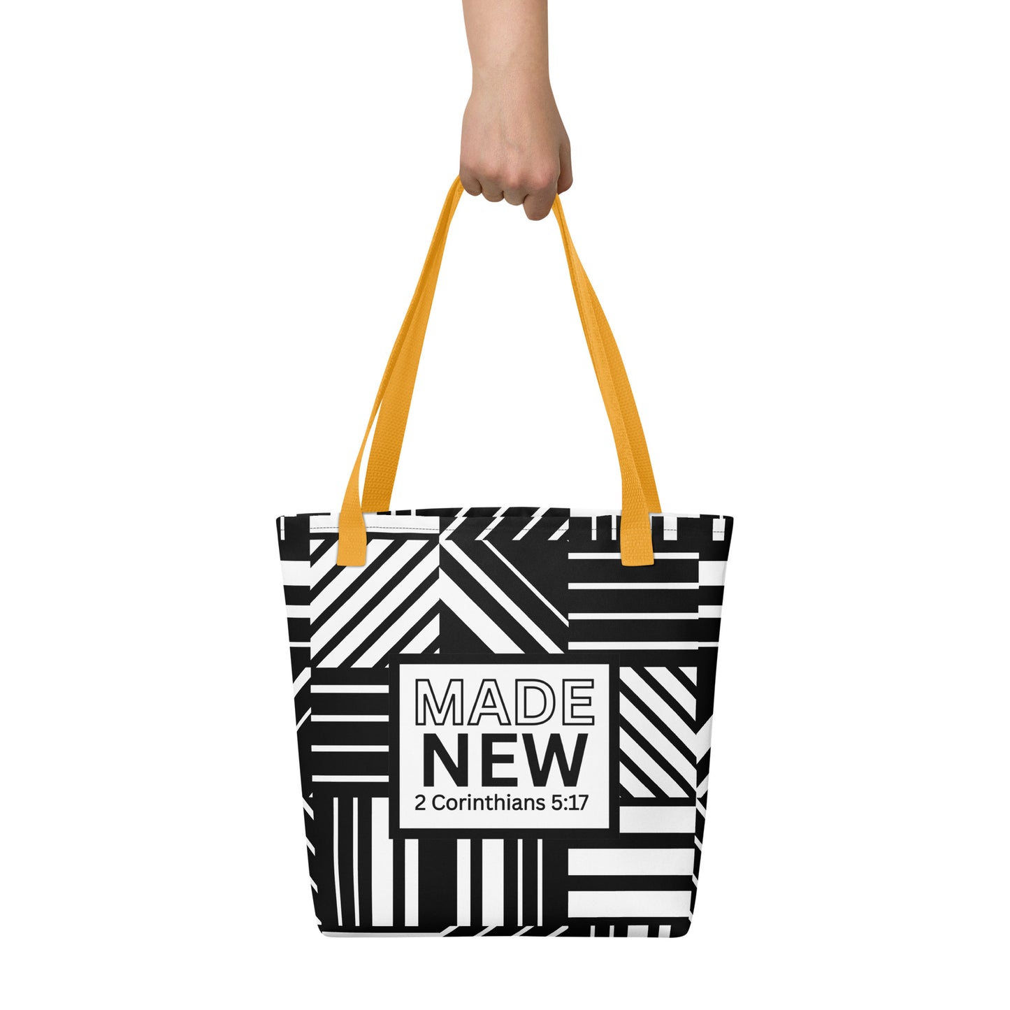 Tote bag carried by hand with yellow straps, featuring the bold black-and-white pattern and the “MADE NEW — 2 Corinthians 5:17” label.