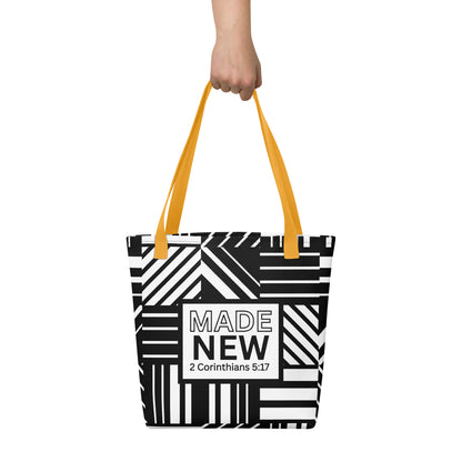 Tote bag carried by hand with yellow straps, featuring the bold black-and-white pattern and the “MADE NEW — 2 Corinthians 5:17” label.