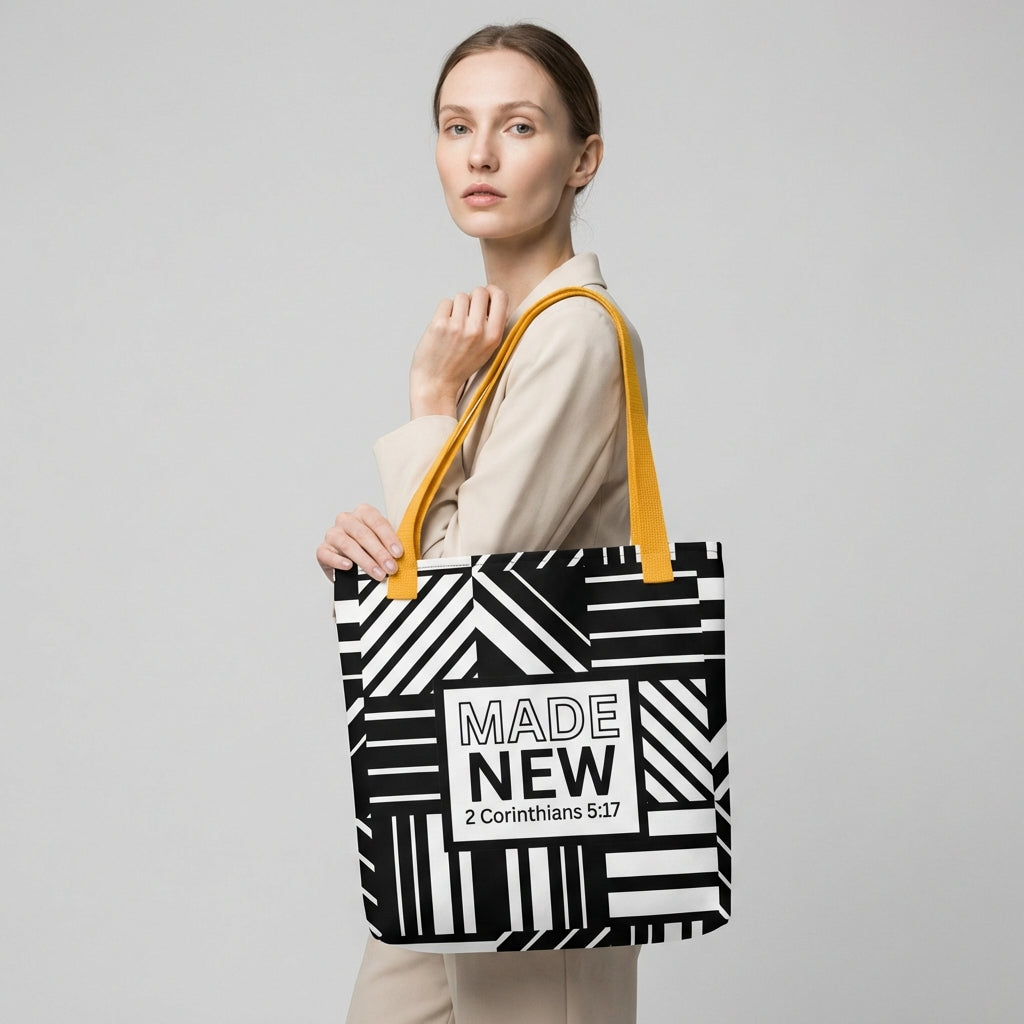 Model carrying a black-and-white geometric patterned tote with yellow handles and the centered “MADE NEW — 2 Corinthians 5:17” design.