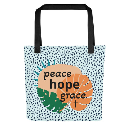 Front view of tote bag with black straps, blue speckled pattern, and tropical leaf design with the words “peace hope grace” and a cross.