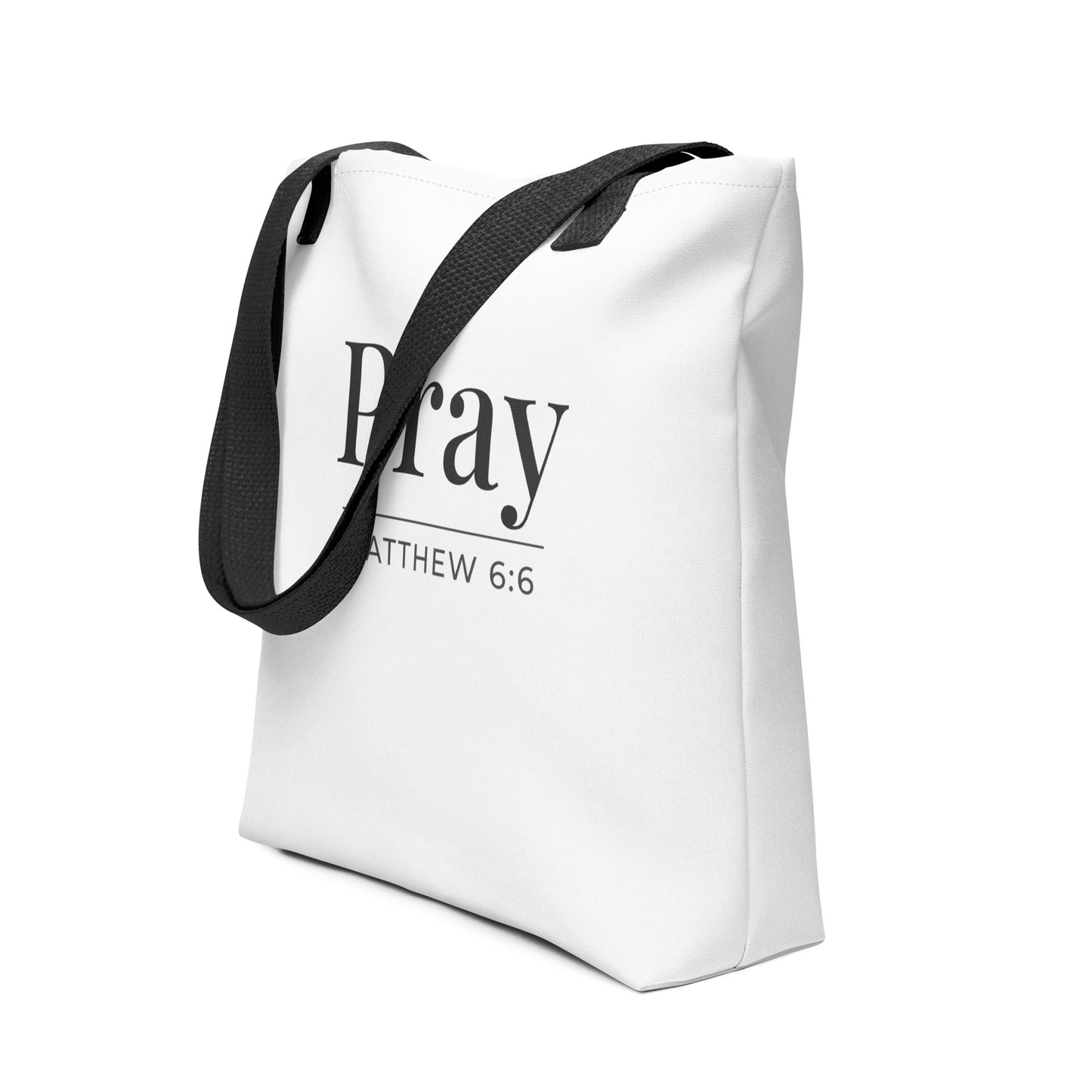 Angled view of a white tote bag with black handles printed with “Pray” in dark gray and the verse “Matthew 6:6.”
