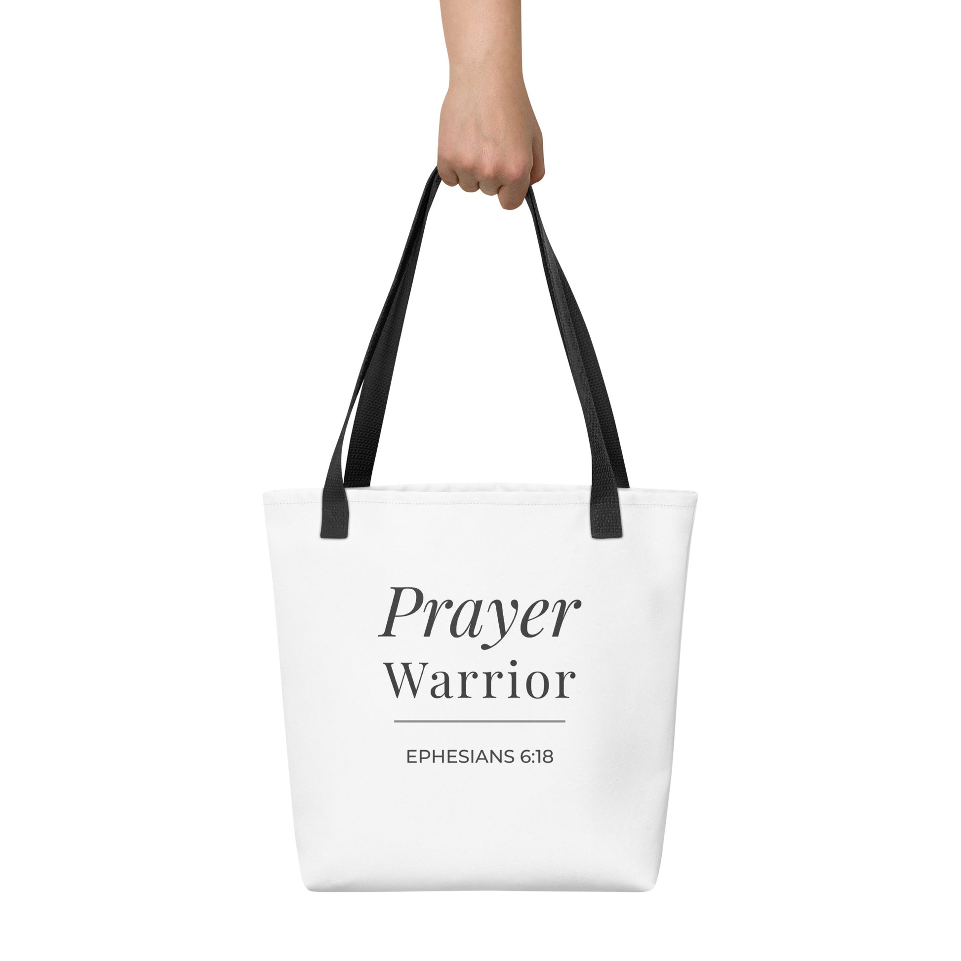 White tote bag held in hand with black handles featuring “Prayer Warrior” and “Ephesians 6:18” in dark gray.