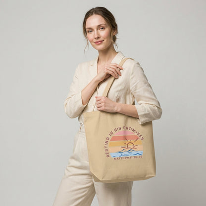 Lifestyle photo of a model holding a cotton tote bag featuring “Resting in His Promises” and “Matthew 11:28–30” with a sunset wave design.