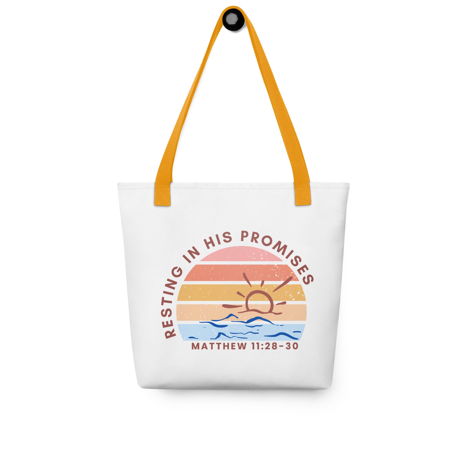 White tote bag with mustard yellow straps hanging on a hook, displaying a sunset and water illustration with “RESTING IN HIS PROMISES” and “MATTHEW 11:28–30.”