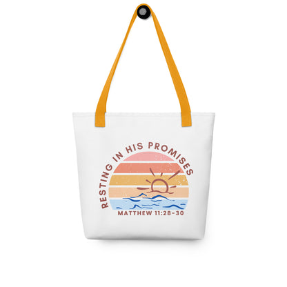 White tote bag with mustard yellow straps hanging on a hook, displaying a sunset and water illustration with “RESTING IN HIS PROMISES” and “MATTHEW 11:28–30.”