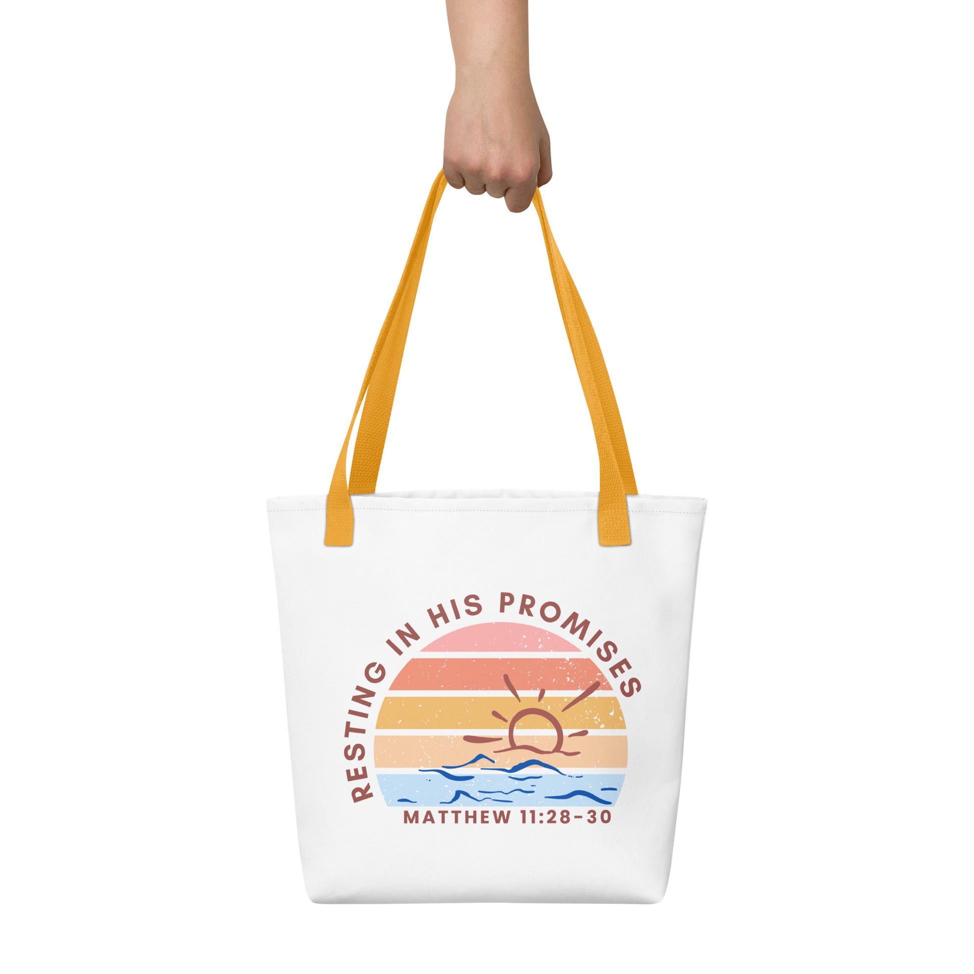 Tote bag held by hand with yellow straps, featuring a retro sunset graphic over blue waves and the Bible verse reference “MATTHEW 11:28–30” under “RESTING IN HIS PROMISES.”