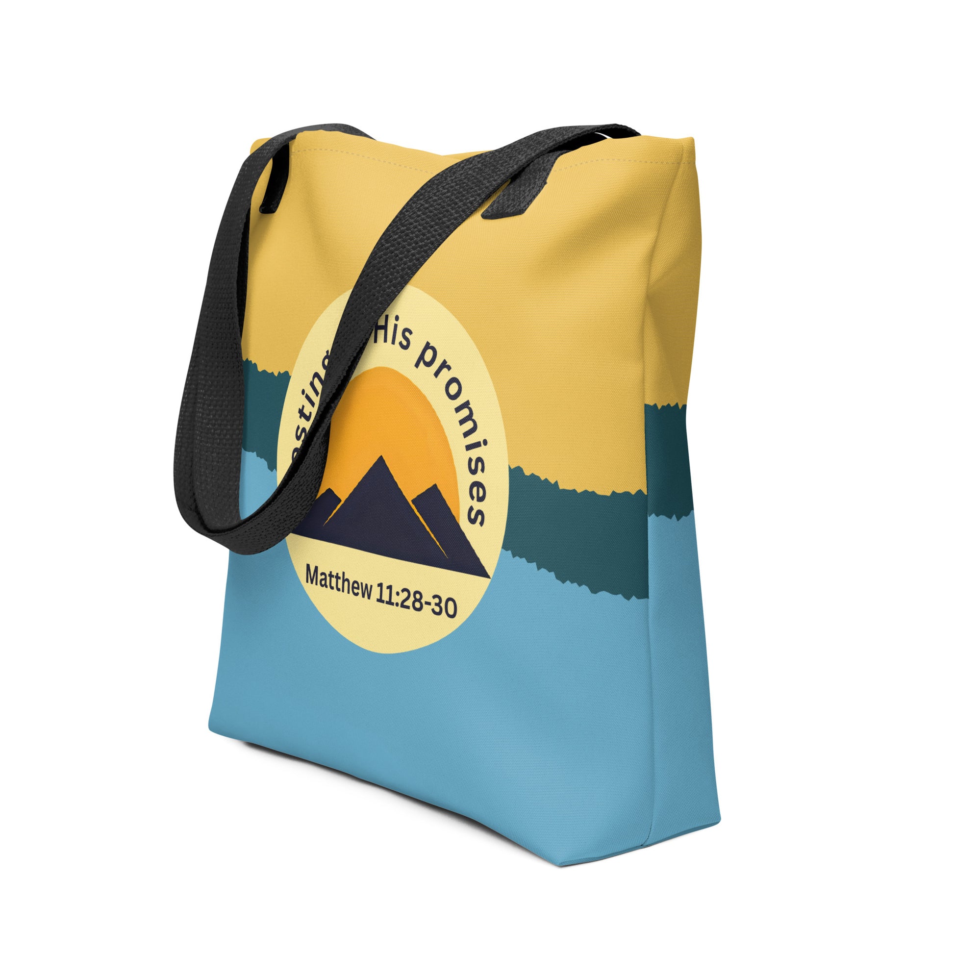 Angled view of tote bag with black handles, yellow-to-blue color block, and “resting in His promises” mountain design with Matthew 11:28–30.