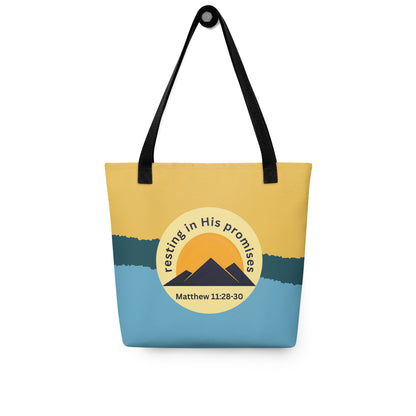 Tote bag hanging on a hook with black straps, yellow and blue background, and “resting in His promises” mountain graphic with Matthew 11:28–30.