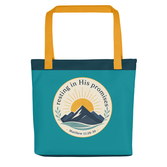 Front view of a teal Christian tote bag with yellow handles, a mountain and sunrise design, and the text “Resting in His Promises Matthew 11:28-30.”