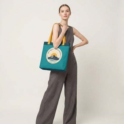 Model carrying a teal Christian tote bag with yellow handles and a faith-inspired mountain design featuring Matthew 11:28-30.