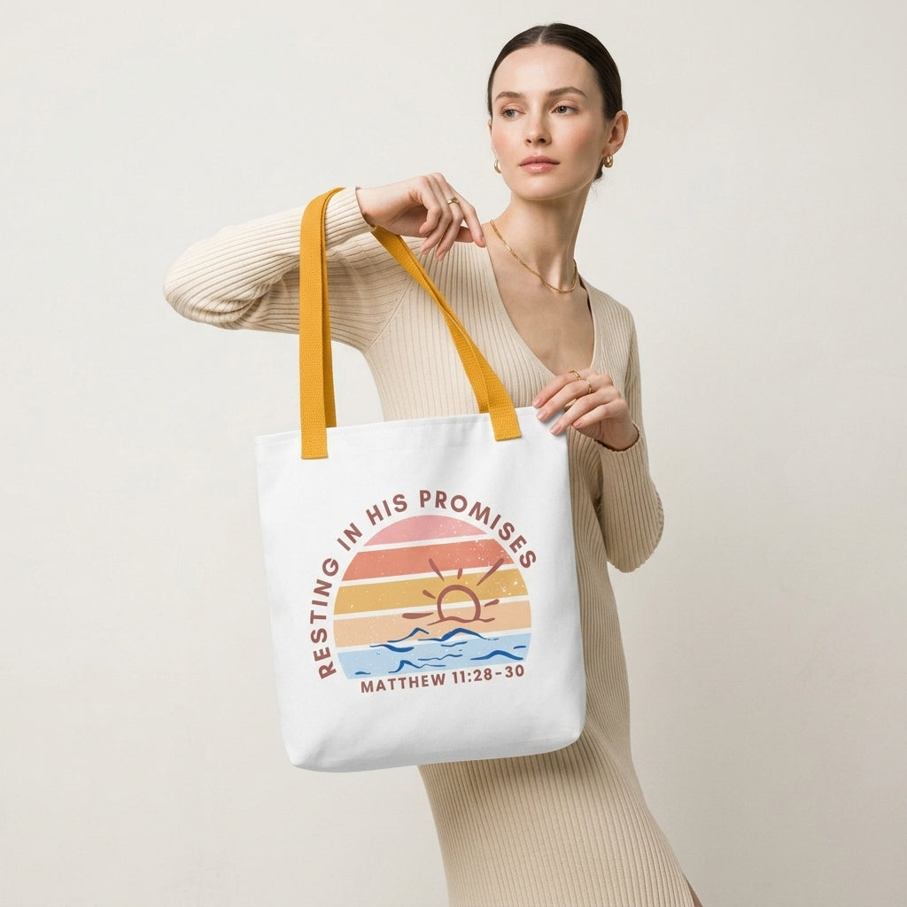 Model carrying a white tote with mustard yellow straps, featuring a retro sunset ocean design and the message “RESTING IN HIS PROMISES” (Matthew 11:28–30) on the front.
