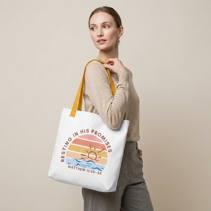 Model carrying a white tote with mustard yellow straps, featuring a retro sunset ocean design and the message “RESTING IN HIS PROMISES” (Matthew 11:28–30) on the front.