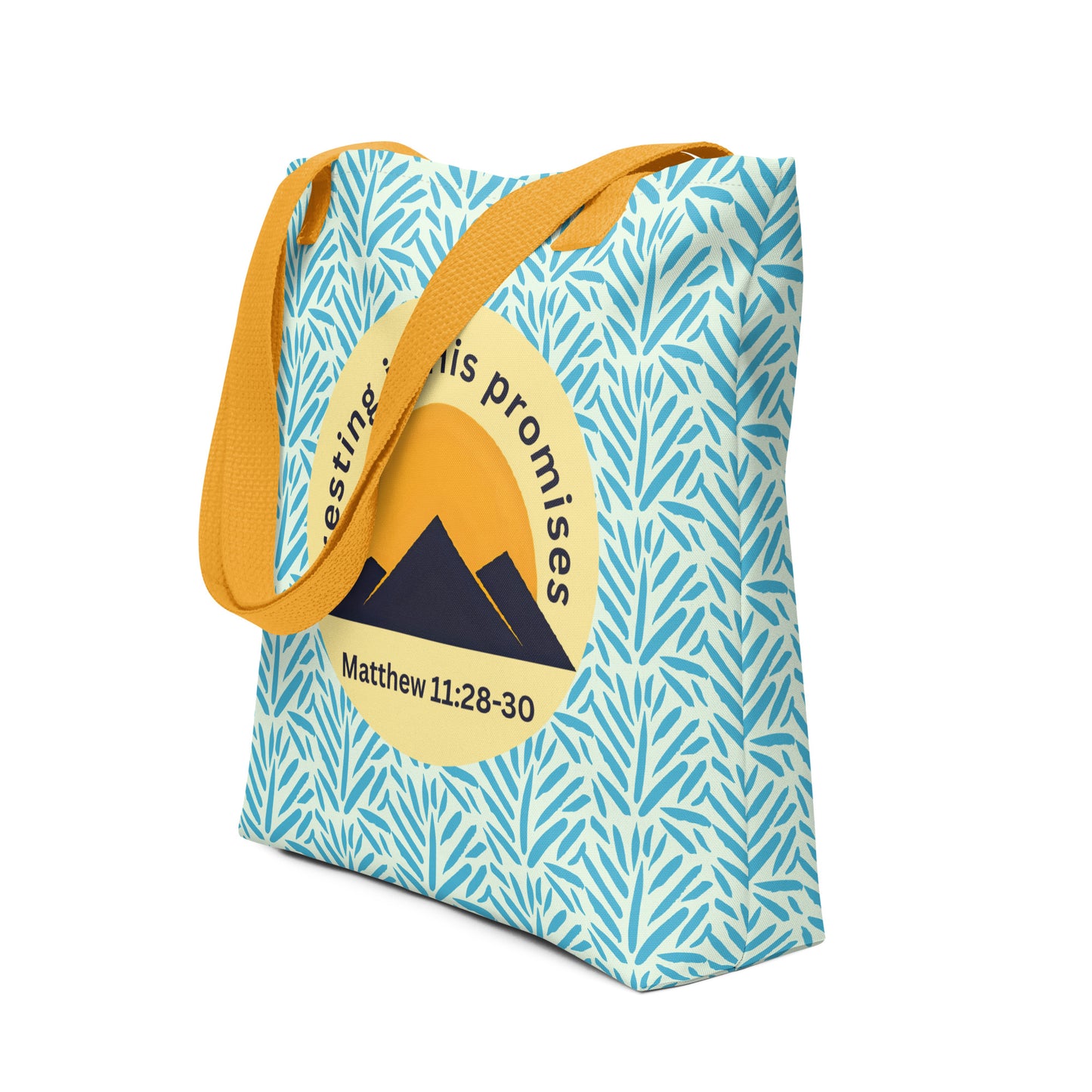 Angled view of “Resting in His Promises” Matthew 11:28–30 tote bag with yellow straps, blue botanical print, and circular mountain sunset design.