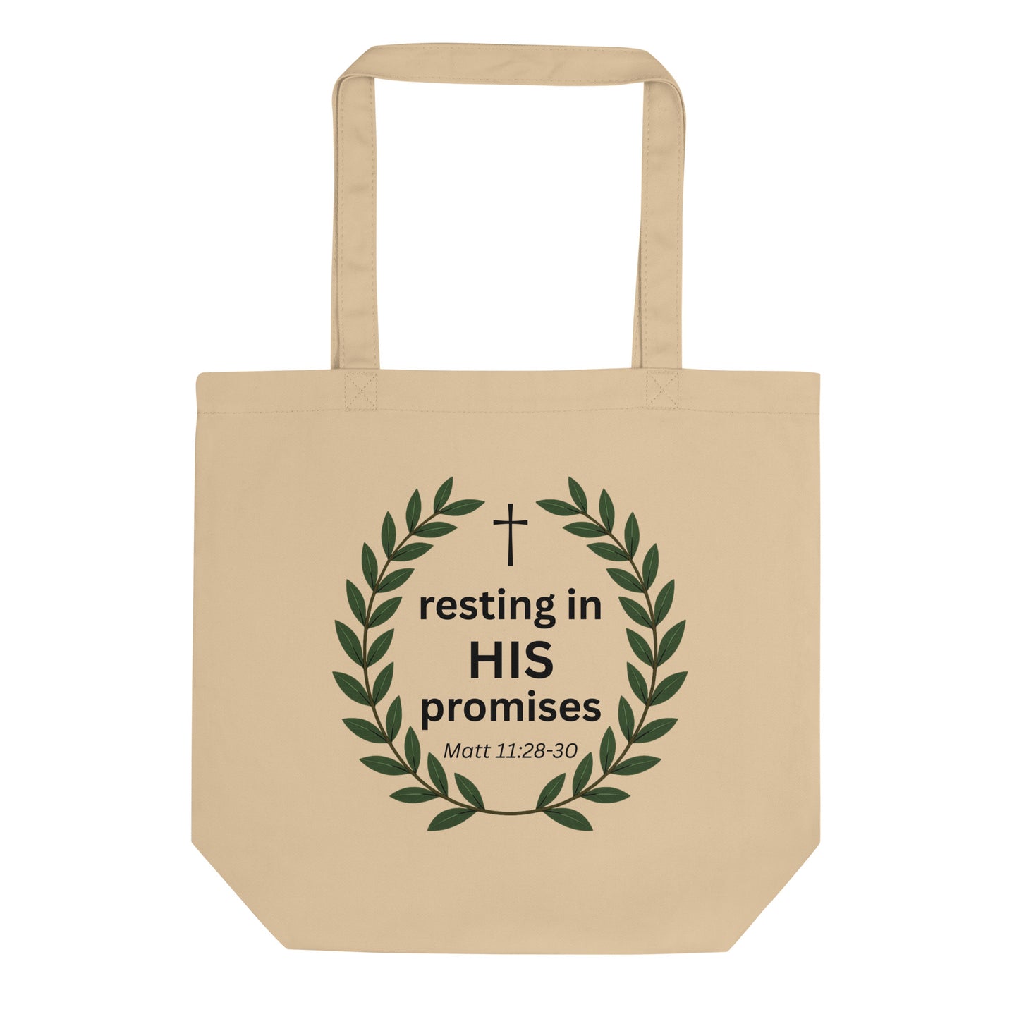 Natural cotton tote bag featuring a green leafy wreath with a small cross and the text “resting in HIS promises” (Matt 11:28–30).
