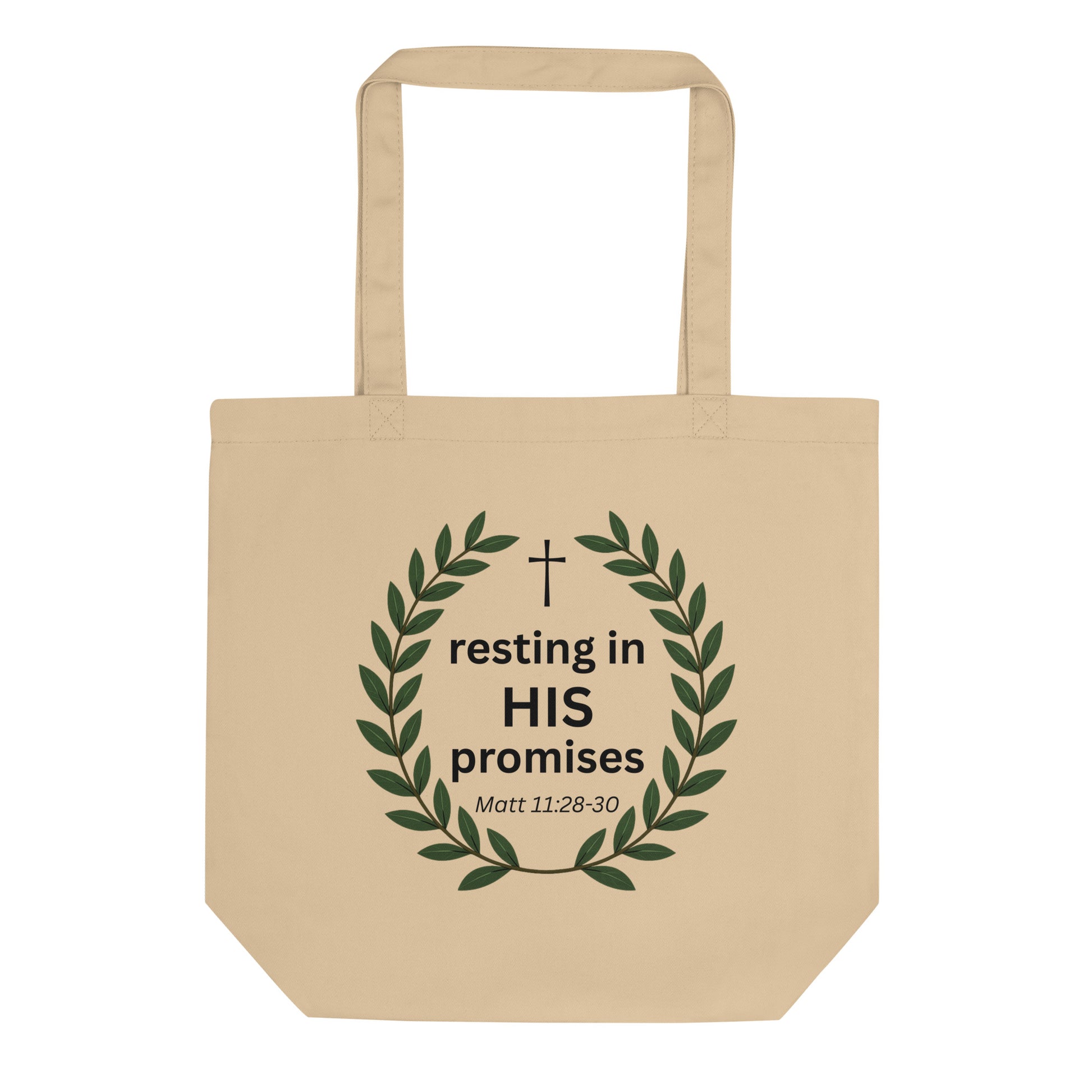 Natural cotton tote bag featuring a green leafy wreath with a small cross and the text “resting in HIS promises” (Matt 11:28–30).