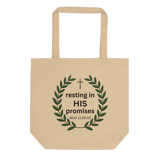 Natural cotton tote bag featuring a green leafy wreath with a small cross and the text “resting in HIS promises” (Matt 11:28–30).