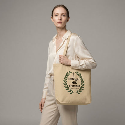 Model holding a natural cotton tote bag featuring a leafy wreath, cross, and “resting in HIS promises” (Matt 11:28–30) design.
