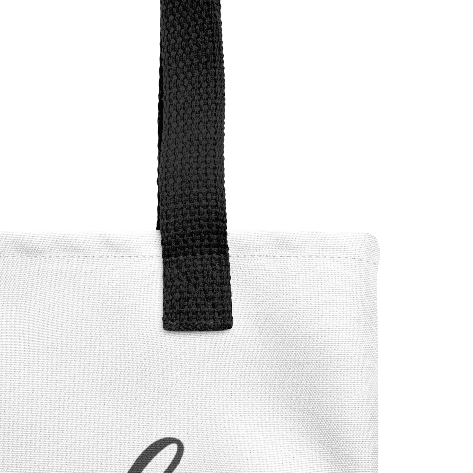 Close-up of the white tote fabric and black strap, highlighting the stitching, textured canvas, and strap weave detail.