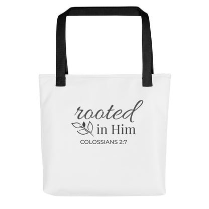 Front view of a white tote bag with black handles featuring “rooted in Him” and “Colossians 2:7” in dark gray with a leaf design.