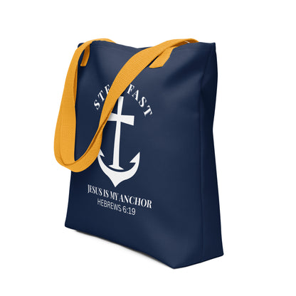 Angled view of the navy tote with yellow handles, showing the white anchor cross design with “STEADFAST” arched above and “JESUS IS MY ANCHOR” (Hebrews 6:19) underneath.