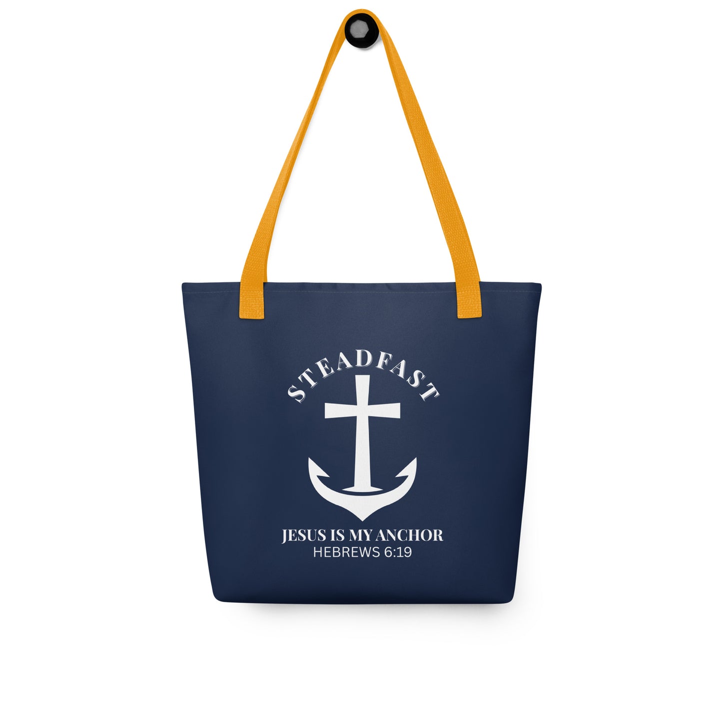 Navy blue tote bag with mustard yellow straps hanging on a hook, displaying a white anchor-and-cross emblem with “STEADFAST” and “JESUS IS MY ANCHOR” (Hebrews 6:19).