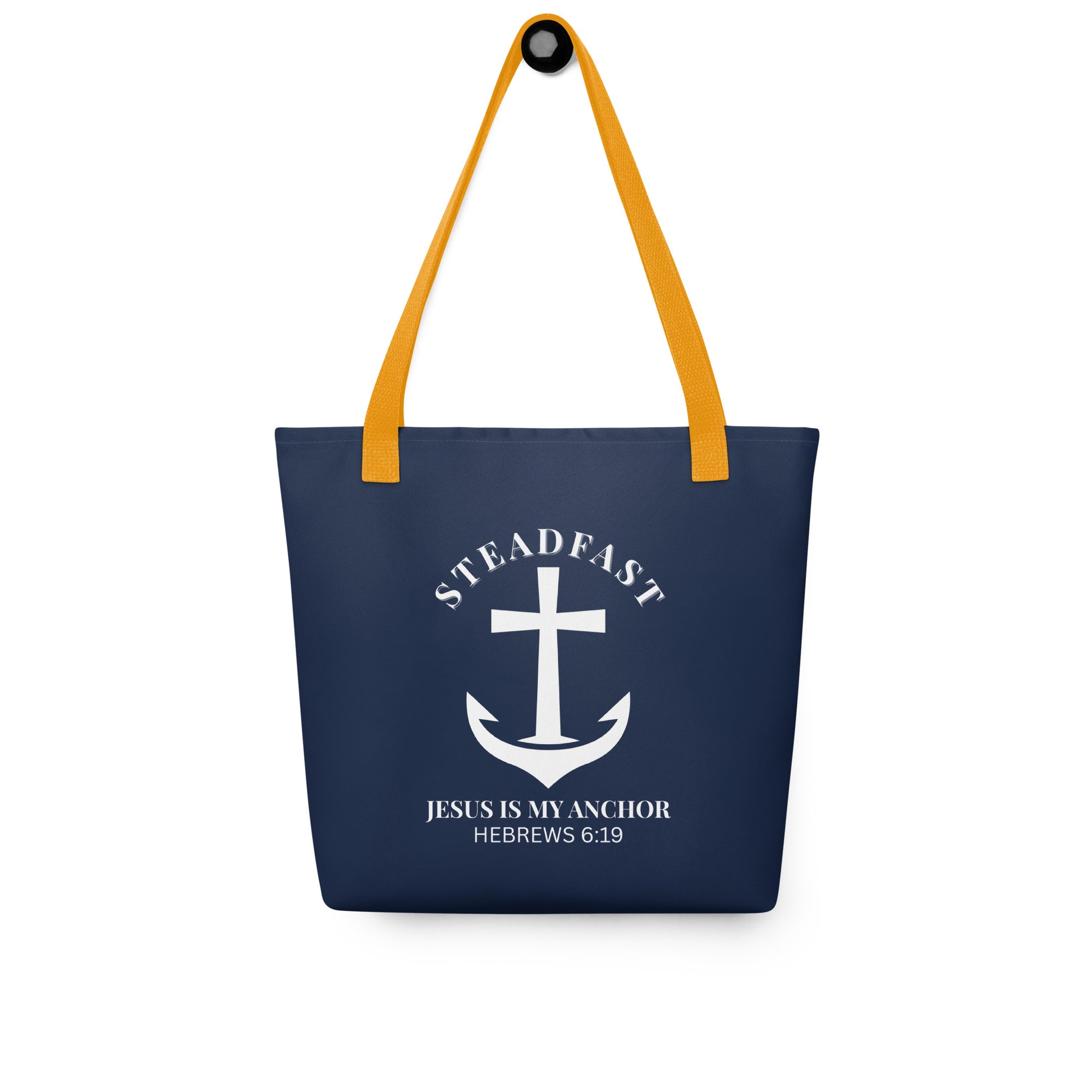 Navy blue tote bag with mustard yellow straps hanging on a hook, displaying a white anchor-and-cross emblem with “STEADFAST” and “JESUS IS MY ANCHOR” (Hebrews 6:19).
