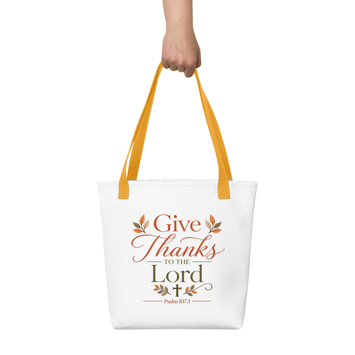 Christian Thanksgiving tote bag being held, featuring Psalm 107:1, fall leaves, a cross, and mustard yellow handles.