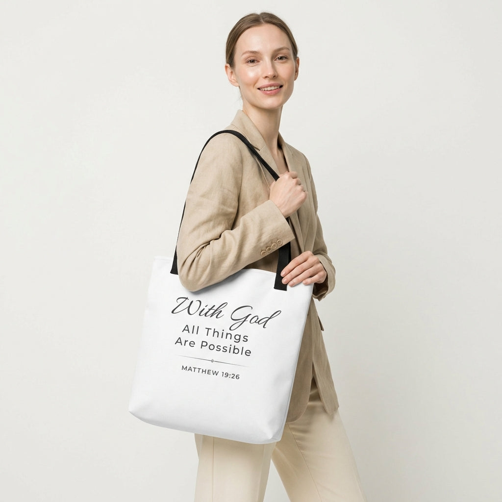 Lifestyle photo of a model holding a white tote bag with black handles featuring “With God all things are possible” and “Matthew 19:26” in dark gray.