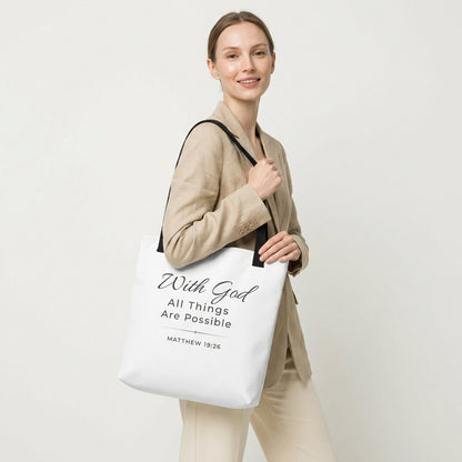 Lifestyle photo of a model holding a white tote bag with black handles featuring “With God all things are possible” and “Matthew 19:26” in dark gray.