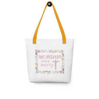 White tote bag hanging on a hook with yellow straps, displaying the “WORSHIP over worry” floral framed graphic with a cross.