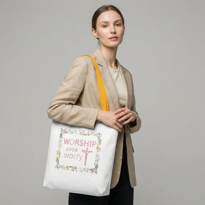 Lifestyle shot of a model wearing a white tote with mustard-yellow straps and a floral framed “WORSHIP over worry” cross design.