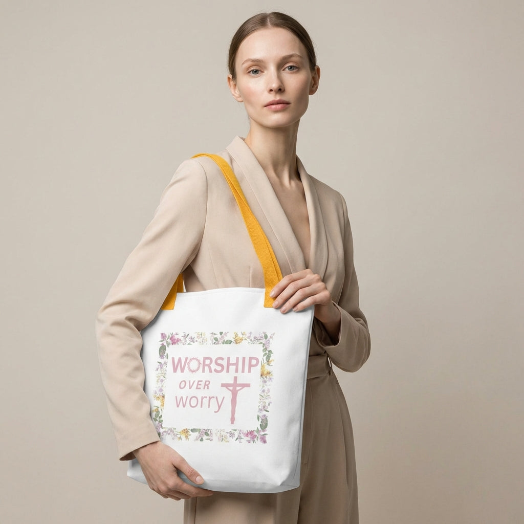 Lifestyle shot of a model wearing a white tote with mustard-yellow straps and a floral framed “WORSHIP over worry” cross design.