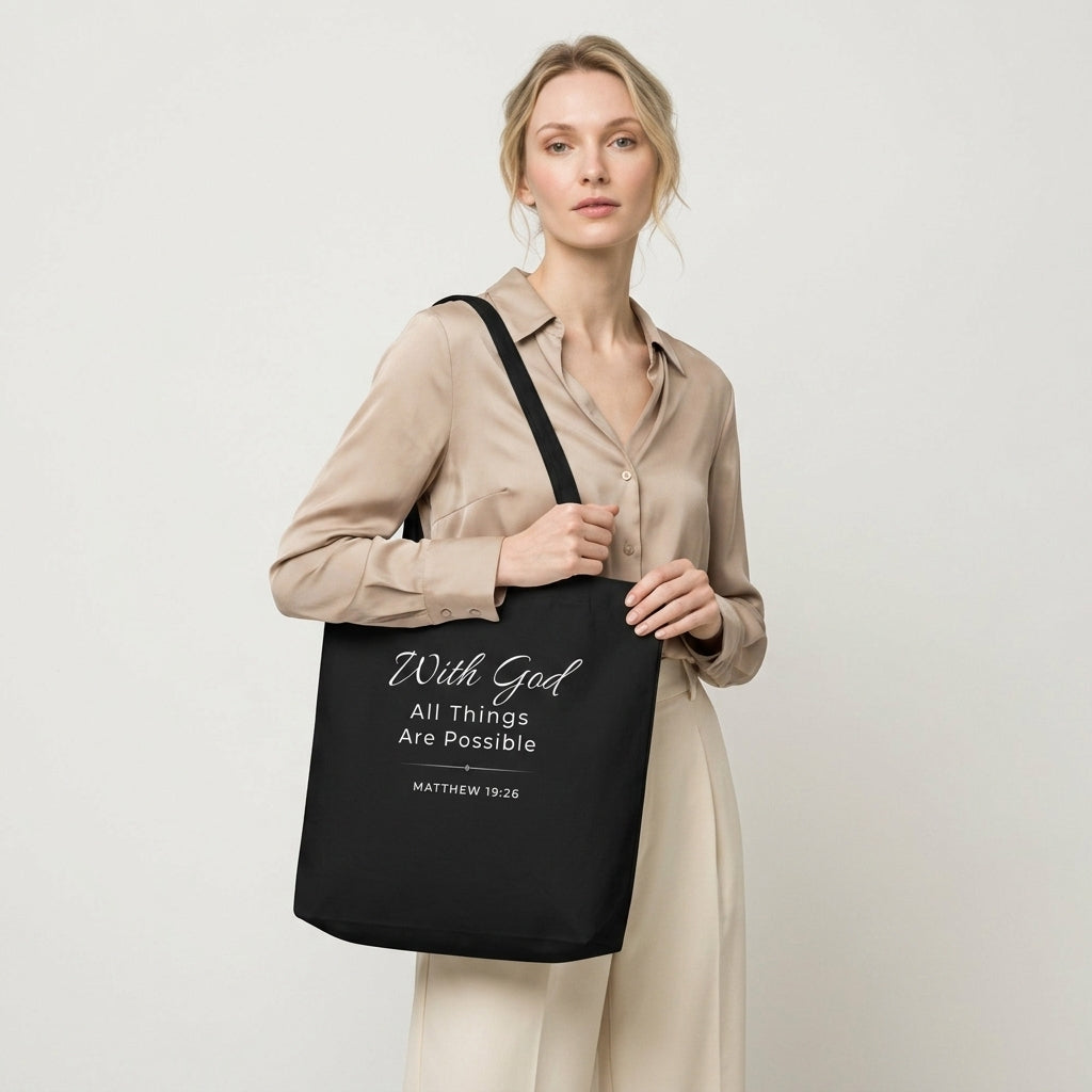Model carrying a black cotton Christian tote bag with matching black handles and a white “With God All Things Are Possible” Matthew 19:26 design.